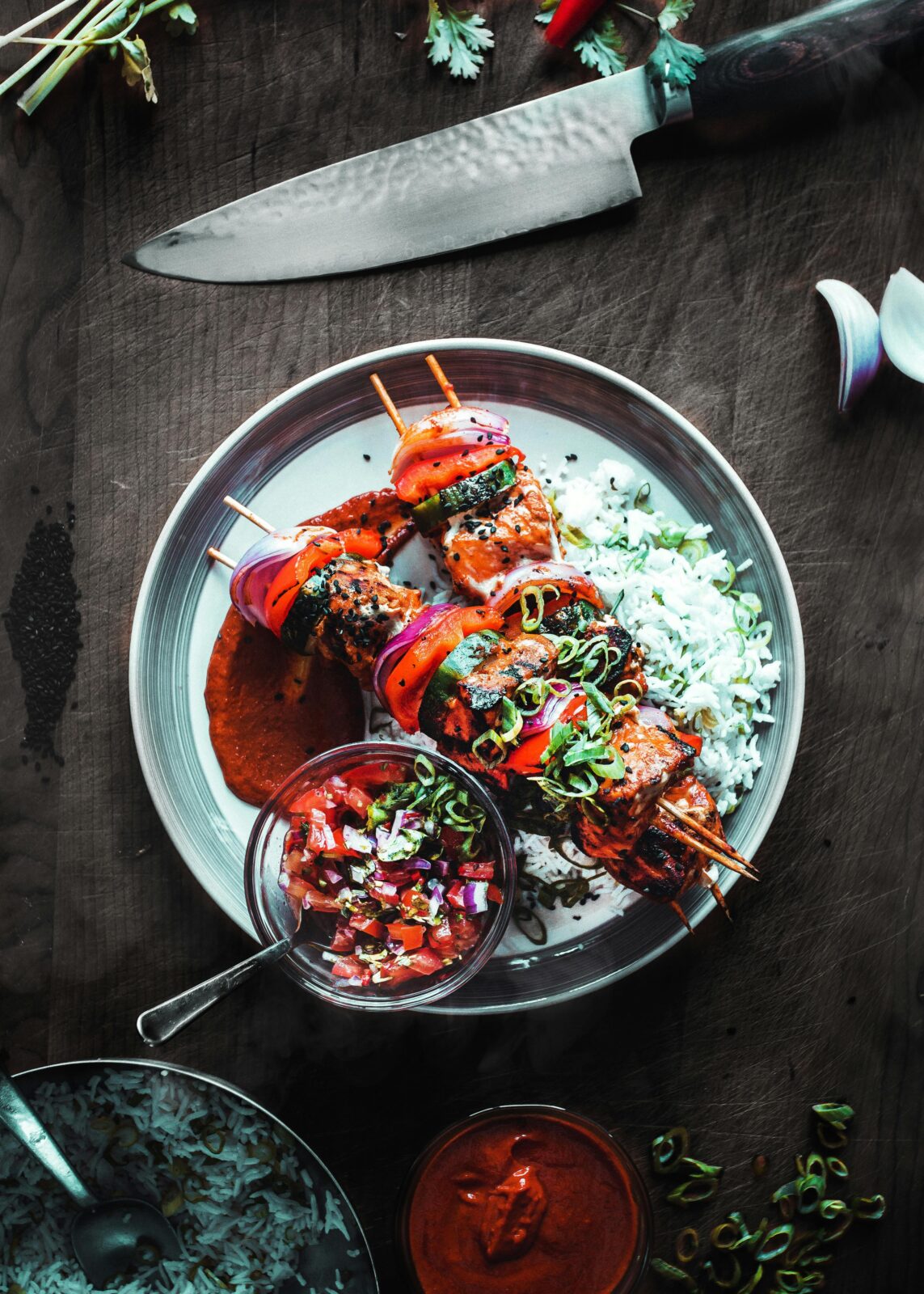 Delicious grilled skewers with rice and salsa served on a wooden table.