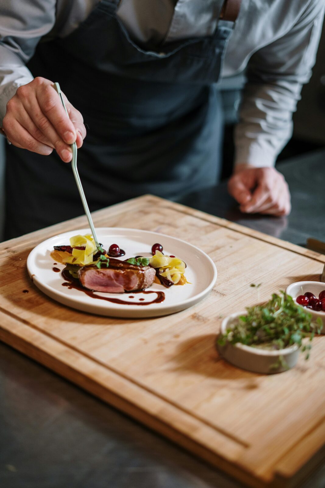 Chef meticulously plates a gourmet dish on a wooden board in a professional kitchen setting.